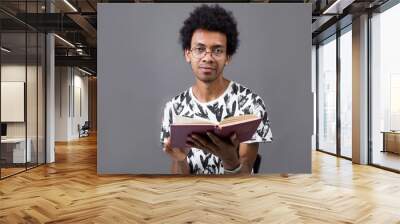 Portrait of a curly African man with glasses on a gray background holding a book Wall mural