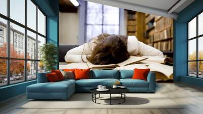 Tired girl in the reading room of the library to prepare for the exam falling asleep on an open book Wall mural