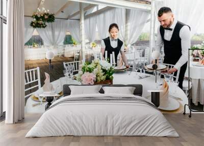 Two male and female waiters serve tableware on the table in the restaurant Wall mural