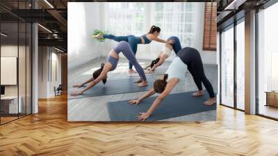 Three attractive beautiful Asian women whit their trainers practice the pose during their yoga class in a gym. Two women practice yoga together. Wall mural