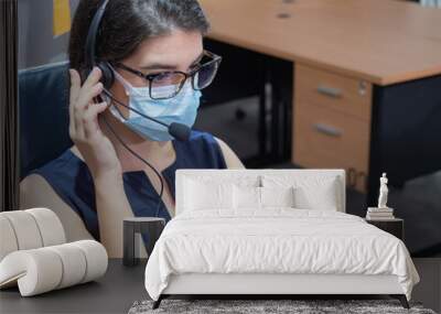 Young caucasian women call center wear headset and mask working with laptop while consulting customers with online problems. Customer service executive team working at office Wall mural