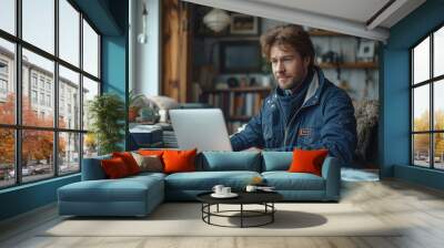 A man in blue work clothes is typing on a laptop at a desk Wall mural