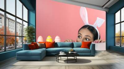 Beautiful young woman with pink bunny ears and Easter eggs on pink background. Minimal Easter concept. Wall mural