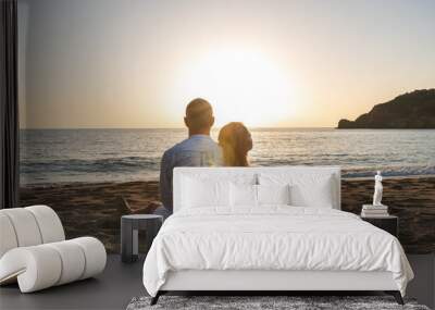 Happy couple in love, is seating on the beach during sunset or sunrise. Summer vacations. Wall mural