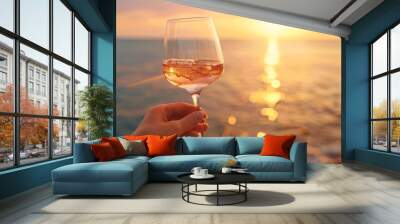 Woman hand holding glass of rose wine with sea and sunset at background Wall mural