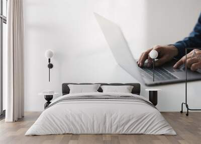 Cropped shot of young businessman hand typing on laptop computer while working in white modern office room. Wall mural