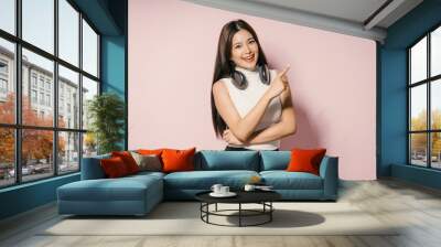 Smiling Young Woman with Headphones Pointing to the Side Against Pink Background Wall mural