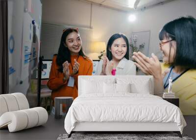 Three young businesswomen are clapping their hands together while standing in front of a whiteboard with graphs and charts. They are celebrating a successful brainstorming session Wall mural