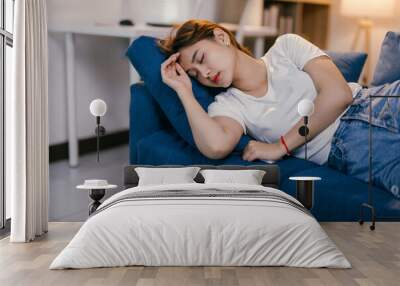 Tired but content young woman peacefully sleeps on a comfortable blue sofa in a cozy living room, embodying quiet solitude in a serene home setting Wall mural