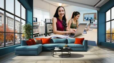 Two young asian businesswomen are working on laptops in a modern office, analyzing financial data and collaborating on a project Wall mural