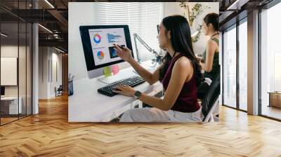 Two young businesswomen are analyzing charts and graphs on a computer screen, collaborating on a project in their bright and modern office Wall mural