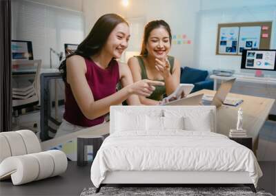 Two young businesswomen are smiling while working together on a laptop and pointing at the screen during a productive day at the office Wall mural