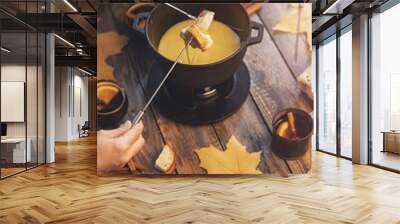 Girl cooks gourmet Swiss fondue dinner with cheese on fire, autumn wooden background with maple leaves. Top view, flat lay Wall mural