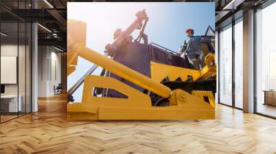 Industrial portrait of working man, excavator driver climbs into cab to perform work on construction site Wall mural