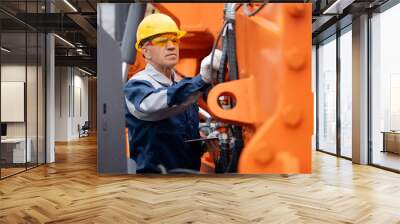 Mechanic repairing hydraulic hose in drilling machine, exploration drilling. Adult man in hard hat industrial worker. Wall mural