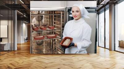 Portrait young woman in uniform baker hold fresh multigrain bread with seeds on background oven, bakery food free gluten healthy Wall mural