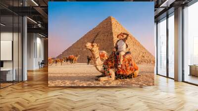 Tourist man with hat riding on camel background pyramid of Egyptian Giza, sunset Cairo, Egypt Wall mural