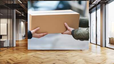 two individuals exchanging a cardboard delivery box in an urban setting, showcasing the concept of package delivery. Wall mural