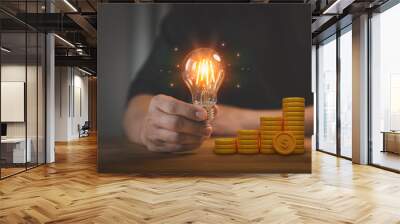 Man hand holding a light bulb and 3d money stack on table. New ideas for savings money, taxes, retirement, working, small business, finance, investment, financial planning, and financial concept. Wall mural