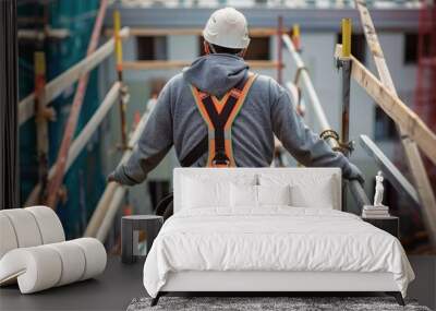 A construction worker on a high scaffold or rooftop, wearing a harness and fall protection gear. Wall mural