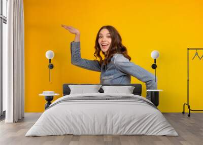 Funny smiling young brunette caucasian woman in denim shirt and jeans dancing with pleasure isolated on yellow background.Indoor portrait excited beautiful curly girl waving hands,celebrating winning Wall mural