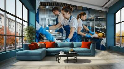 A professional cleaning team working in a restaurant kitchen, three people wearing blue overalls and white shirts and blue gloves. are cleaning the kitchen table Wall mural