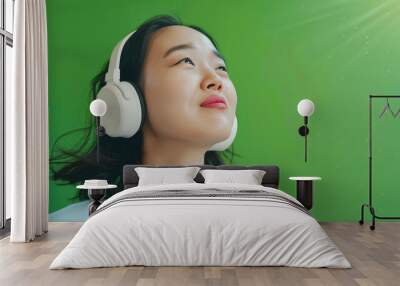 Young Asian woman listening to music with headphones on green background Wall mural