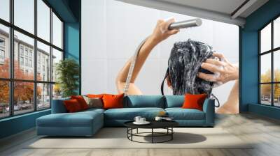 Young woman in shower rinse shampoo foaming with water dripping on hair and body. Taking shower relaxing under warm running water. Female washing her hair and hand to massage head while washing hair. Wall mural