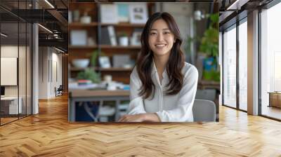 Portrait of young successful Asian businesswoman sitting in office while looking at camera Wall mural