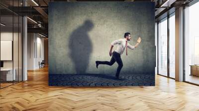 Man running away from his sad gloomy fat shadow on the wall. Wall mural