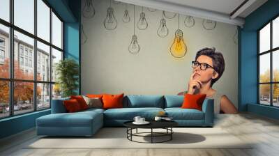 Portrait thinking woman in glasses looking up with light idea bulb above head Wall mural