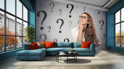 Thinking business woman with glasses looking up on many questions mark Wall mural