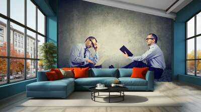 Two men sitting on a floor one reading a book another working on laptop Wall mural