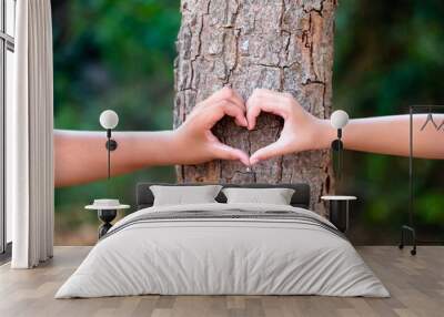 Closeup hands of a boy and a girl join together to make a heart sign on the tree trunk in the forest Wall mural