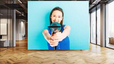 beautiful young woman pointing to the front with a professional hair dryer with blue background. hair care concept. beauty hairdresser Wall mural