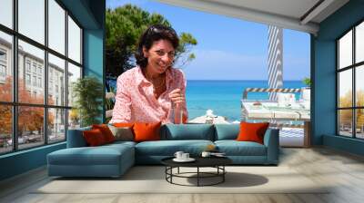 Brunette woman sipping a cocktail juice glass sitting at a beach Wall mural