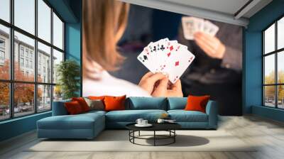 Friends are playing cards together at home. Woman is holding cards in her hands, man in the blurry background. Wall mural