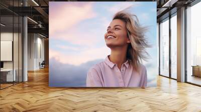 Portrait of young european fashionable female model, shot from the side, smiling, looking to the side, vibrant pastel cloud sky background Wall mural