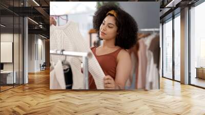 To purchase or not to purchase. Shot of a young woman shopping for clothes inside a store. Wall mural