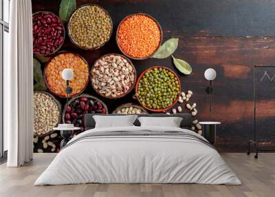 Top view of various bowls of legumes of various types and colors on a dark wooden kitchen table. Healthy food concept and detox or vegan menu. World Pulses Day. Wall mural