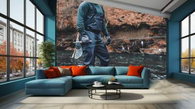 Fisherman fly fishing in river with rod, reel and landing net Wall mural