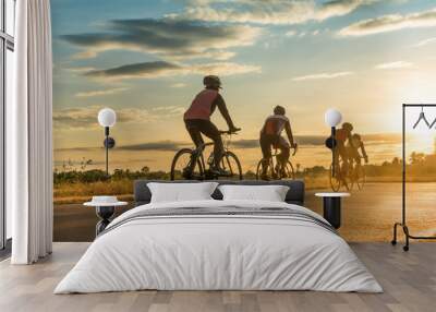 Group of  men ride  bicycles at sunset with sunbeam over silhouette trees background. Wall mural