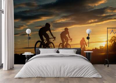 The men ride  bikes at sunset with orange-blue sky background. Abstract Silhouette background concept. Wall mural