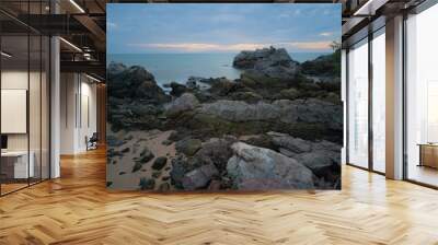 Sunrise/sunset at sea, calm waves and rocky shore. Wall mural