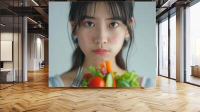 Asian woman on a diet, grimacing at vegetables on her fork, white background Wall mural