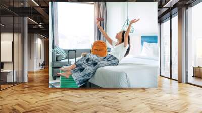 Happy young Asian traveler woman relax on bed in hotel room. Travel alone, summer and holiday concept.	 Wall mural