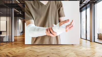 Young man with gauze bandage wrapped around his injured arms, knee at home. Man with hands wrap in medical bandage on white background. First aid, treatment after accident injury. Copy space, closeup Wall mural