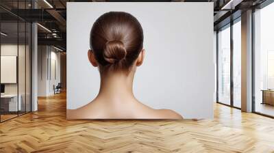 A minimalist, back-view portrait of a woman with her hair elegantly styled in a bun, set against a soft background. The smooth, flawless appearance highlights sophistication and simplicity Wall mural