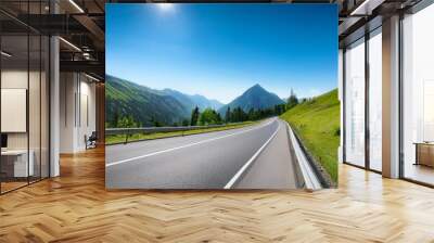 smooth asphalt road winding through green mountains under a clear blue sky Wall mural