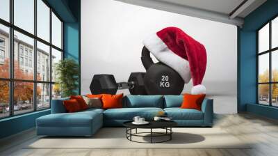 A large black Kettlebell wearing a red  Santa hat with a dumbbell next to it on a plain light gray background  Wall mural